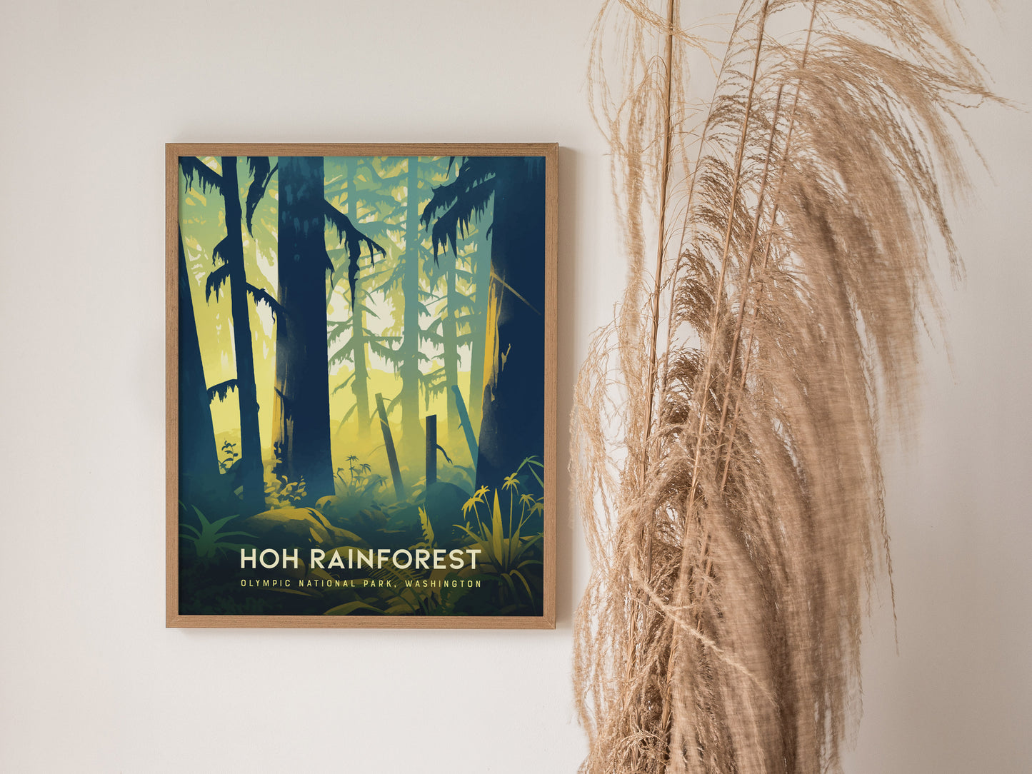 A framed Hoh Rainforest poster is displayed on a light wall next to tall, dried pampas grass. The artwork features a forest scene with silhouetted trees.