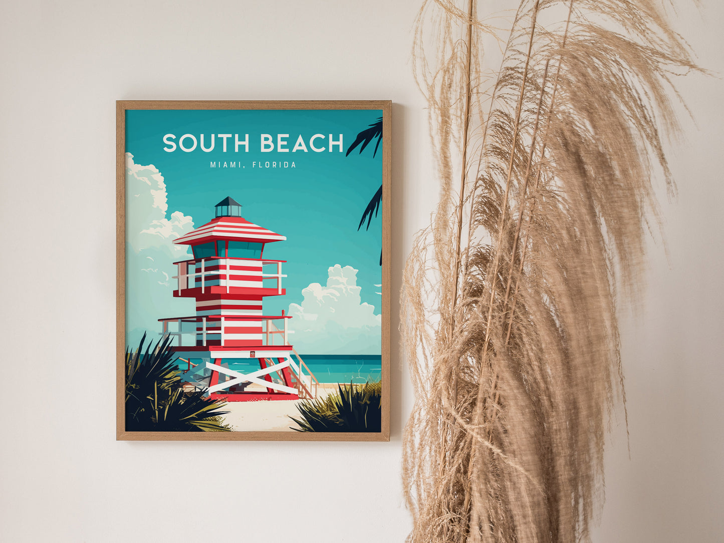 A framed poster of a red and white striped lifeguard tower is displayed against a turquoise sky, with South Beach Miami, Florida written at the top. Tall, dried grass decorates the right side of the scene.