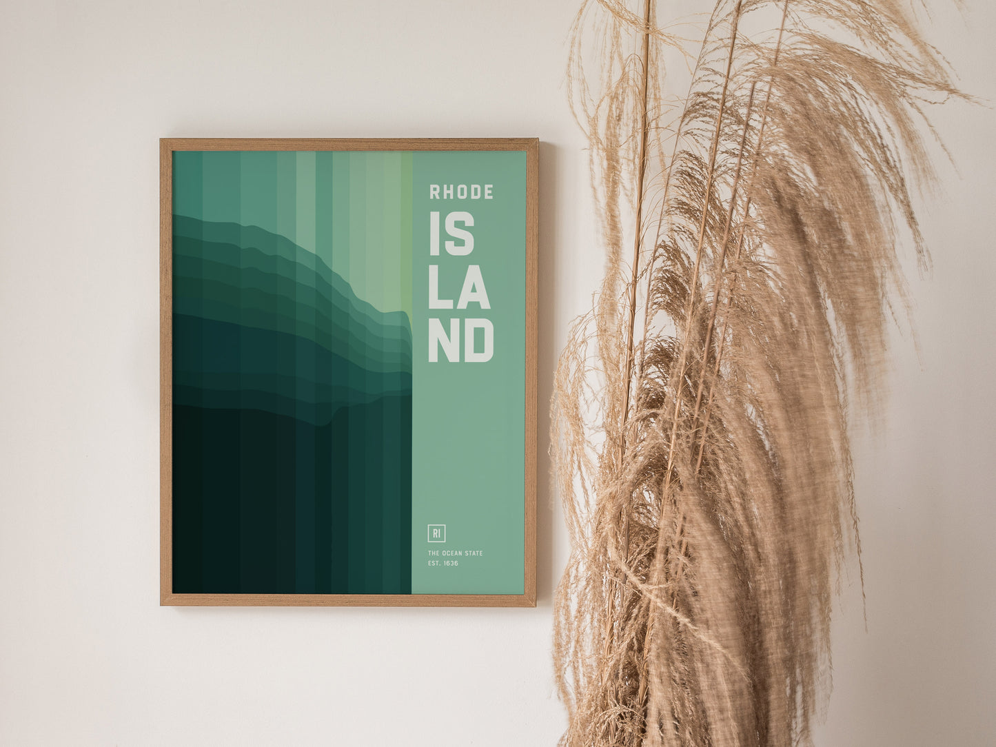 A framed poster titled Rhode Island with abstract green and teal gradients hangs on a wall beside dried pampas grass. The design is minimalist.