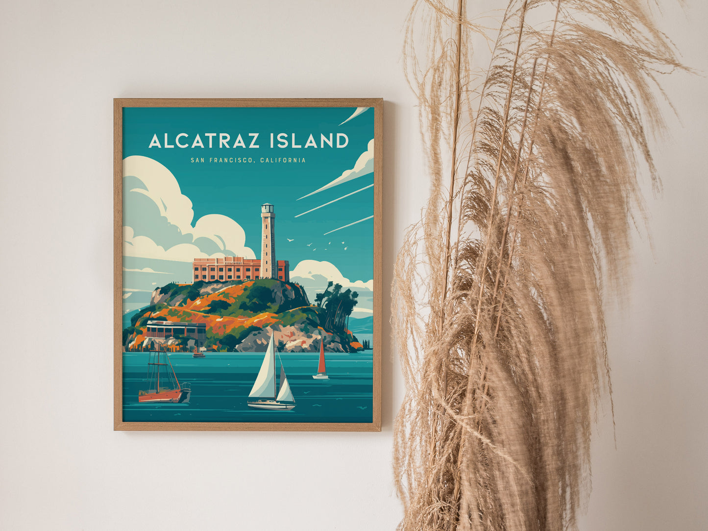 A framed Alcatraz Island poster depicting the historic prison on a rocky island with sailboats in the foreground, set against a vibrant blue sky. Pampas grass decorates the right side.