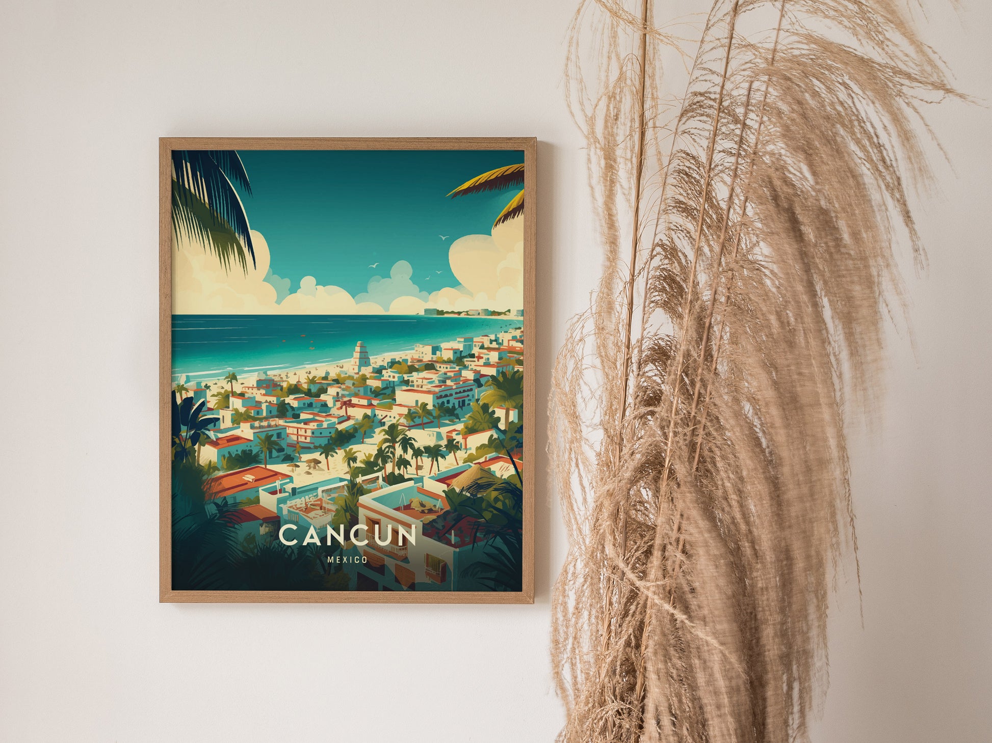 A framed poster of Cancun, Mexico, features vibrant turquoise waters, palm trees, and colorful buildings, depicting a tropical paradise. Its displayed next to tall, dried pampas grass.