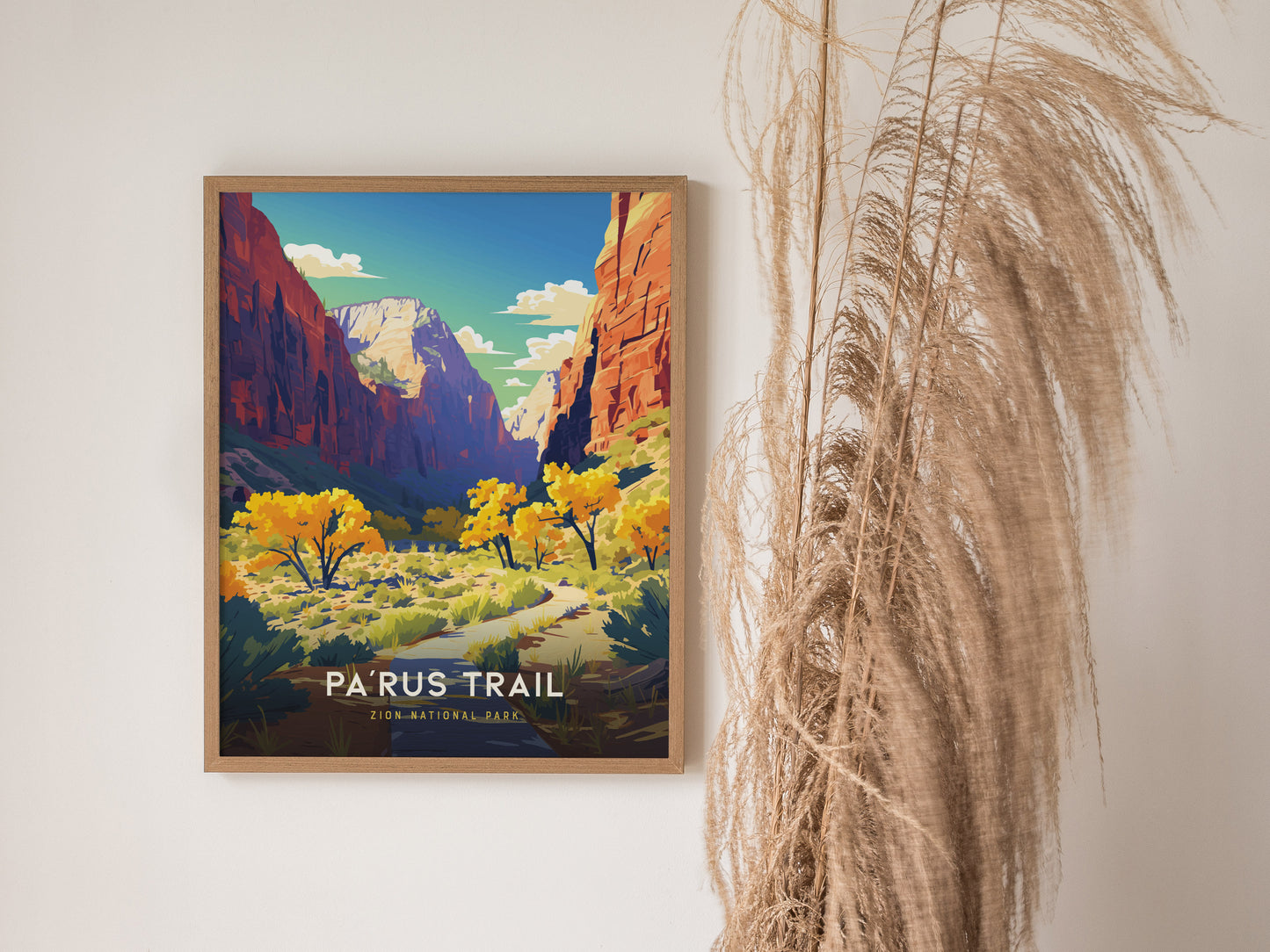 A framed poster of Zion National Parks Parus Trail hangs on a white wall, featuring vibrant autumn trees and towering red cliffs under a blue sky.