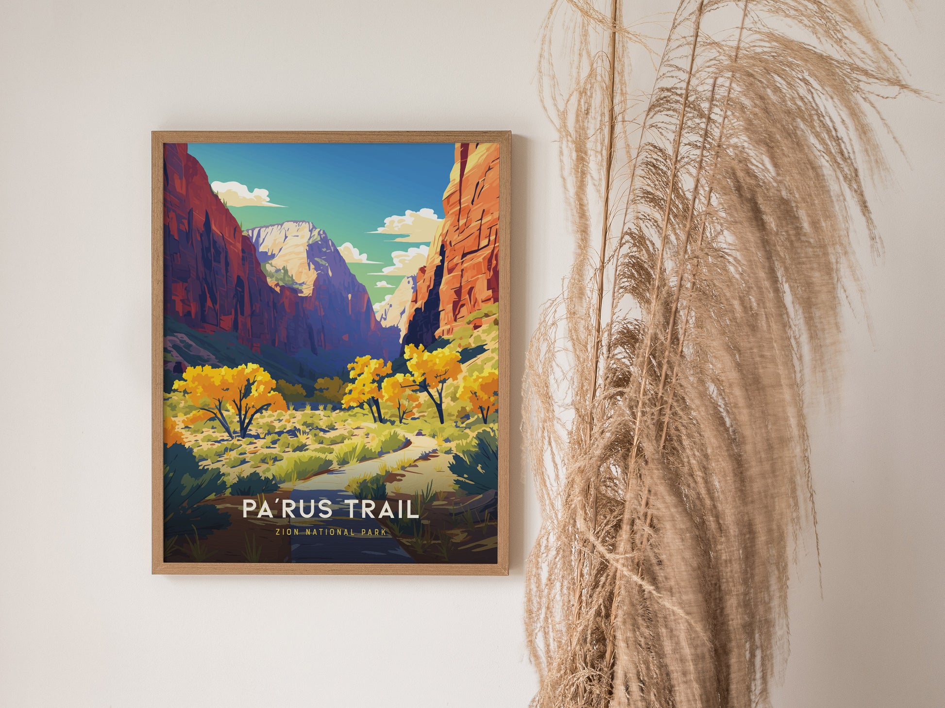 A framed poster of Zion National Parks Parus Trail hangs on a white wall, featuring vibrant autumn trees and towering red cliffs under a blue sky.