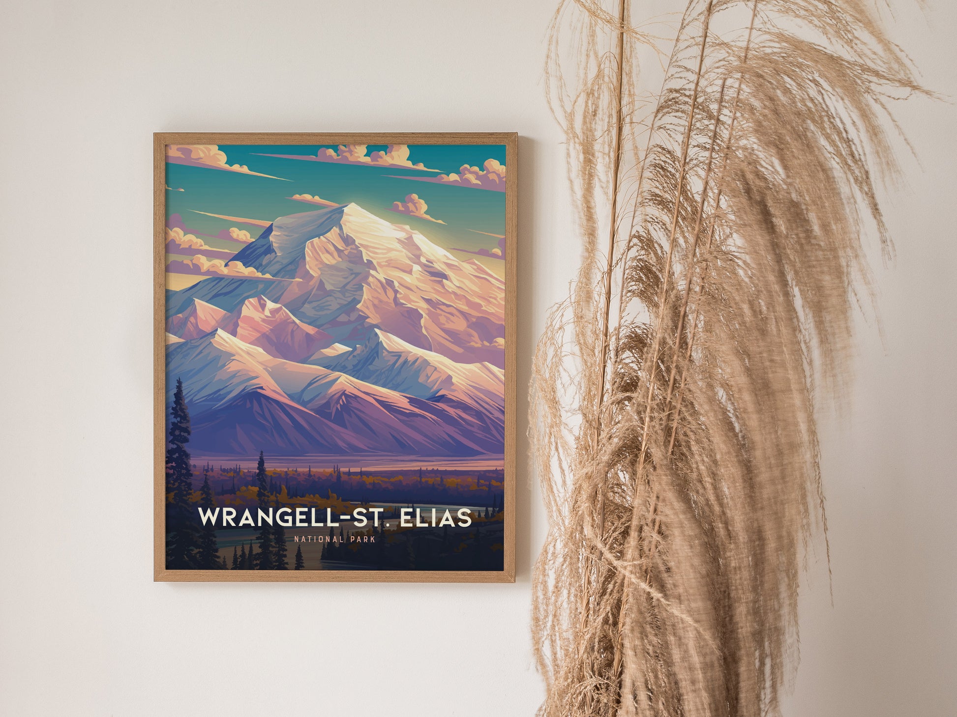 A framed poster of Wrangell-St. Elias National Park features vibrant mountain peaks and a colorful sky. Its displayed on a wall next to tall, dried grass.