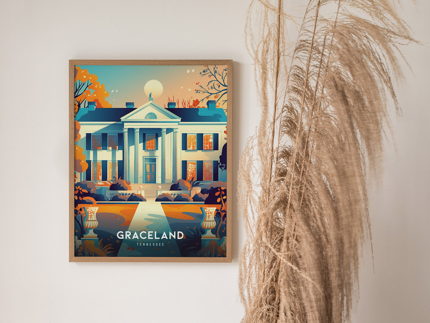 Framed illustration of Graceland with vibrant colors, depicting its iconic façade, hangs on a white wall next to tall, dried ornamental grass.