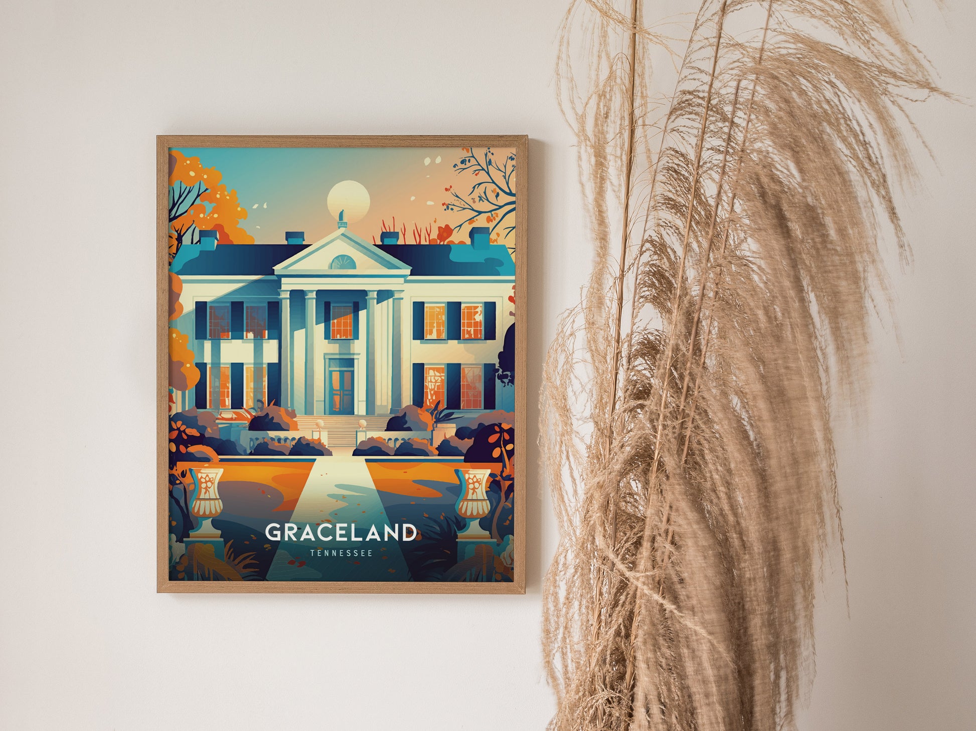 Framed illustration of Graceland with vibrant colors, depicting its iconic façade, hangs on a white wall next to tall, dried ornamental grass.