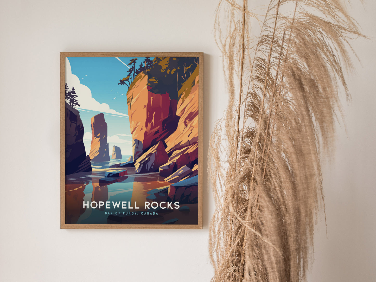 A framed Hopewell Rocks poster featuring colorful cliffs and a serene shoreline is displayed on a wall beside decorative dried plants.