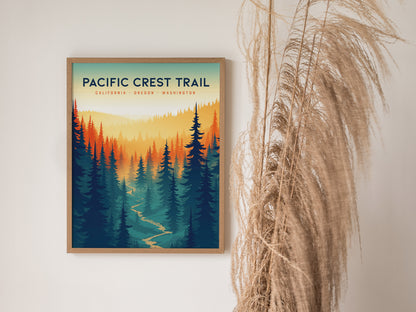 Framed Pacific Crest Trail poster on a white wall, featuring a colorful forest landscape with a winding path. Dried pampas grass decorates the right side of the scene.
