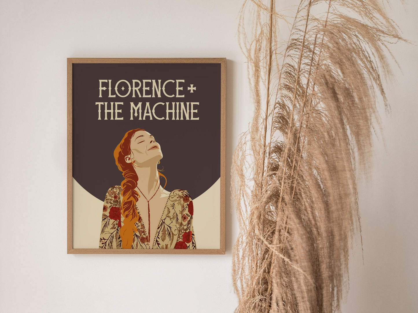 Framed Florence + The Machine poster featuring an illustrated woman with closed eyes and a floral outfit, set against a dark background, beside decorative dried pampas grass.