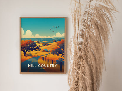A framed poster depicts a vibrant landscape with rolling hills, colorful trees, and birds flying in the sky, titled Hill Country Texas. Tall dried grasses are placed beside it.