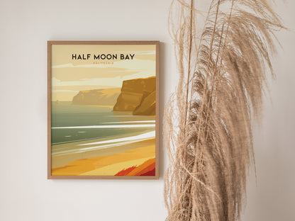 Framed Half Moon Bay, California poster depicting a coastal scene with cliffs and ocean waves, displayed beside tall dried grasses against a white wall.