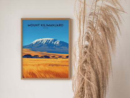 A framed Mount Kilimanjaro poster with a vibrant landscape featuring a snow-capped peak and golden savanna. Dried pampas grass is placed beside the artwork for a decorative touch.