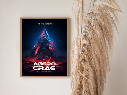 Framed poster featuring a stylized, colorful mountain peak labeled Aggro Crag with Do you have it? text above, next to tall dried grasses against a light wall.
