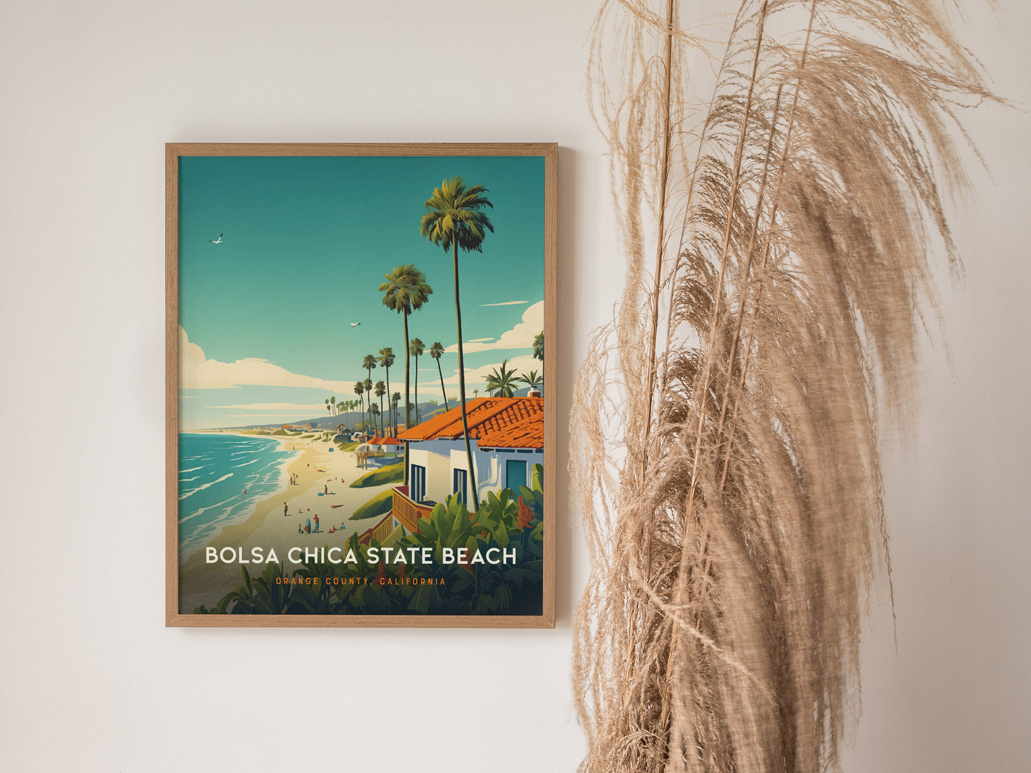 A framed Bolsa Chica State Beach poster hangs on a white wall, depicting a coastal scene with palm trees and a vibrant beach.