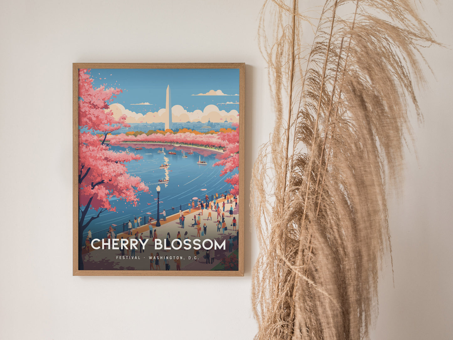 A framed poster depicting Washington D.C.s Cherry Blossom Festival, featuring vibrant pink cherry trees, the Washington Monument, and a lively riverside scene with people and boats. Pampas grass decorates the right side of the wall.