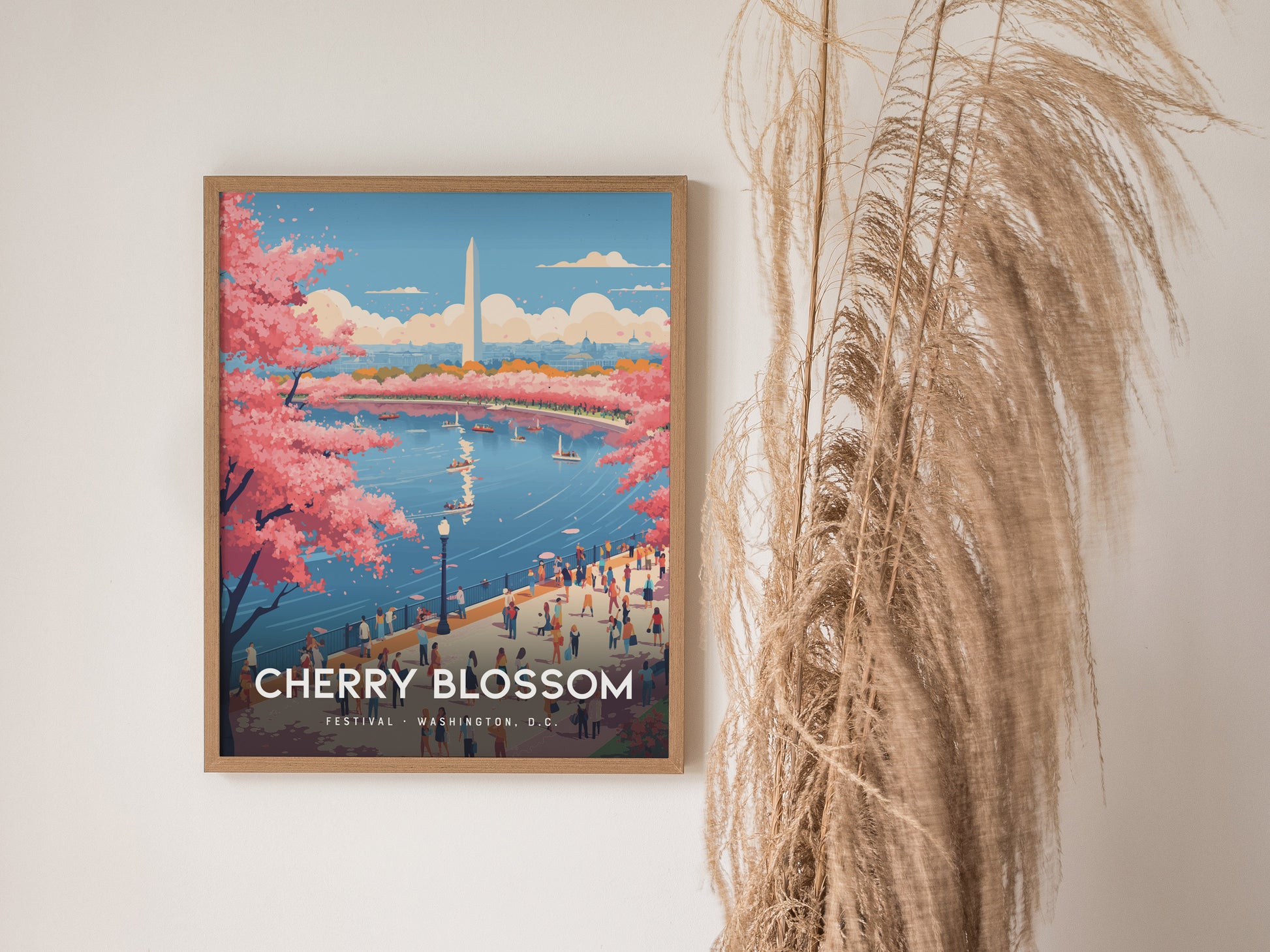 A framed poster depicting Washington D.C.s Cherry Blossom Festival, featuring vibrant pink cherry trees, the Washington Monument, and a lively riverside scene with people and boats. Pampas grass decorates the right side of the wall.