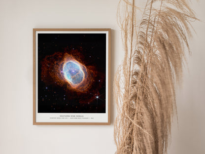 Natural wood framed Southern Ring Nebula space print leaning on a shelf beside plants and neutral accessories