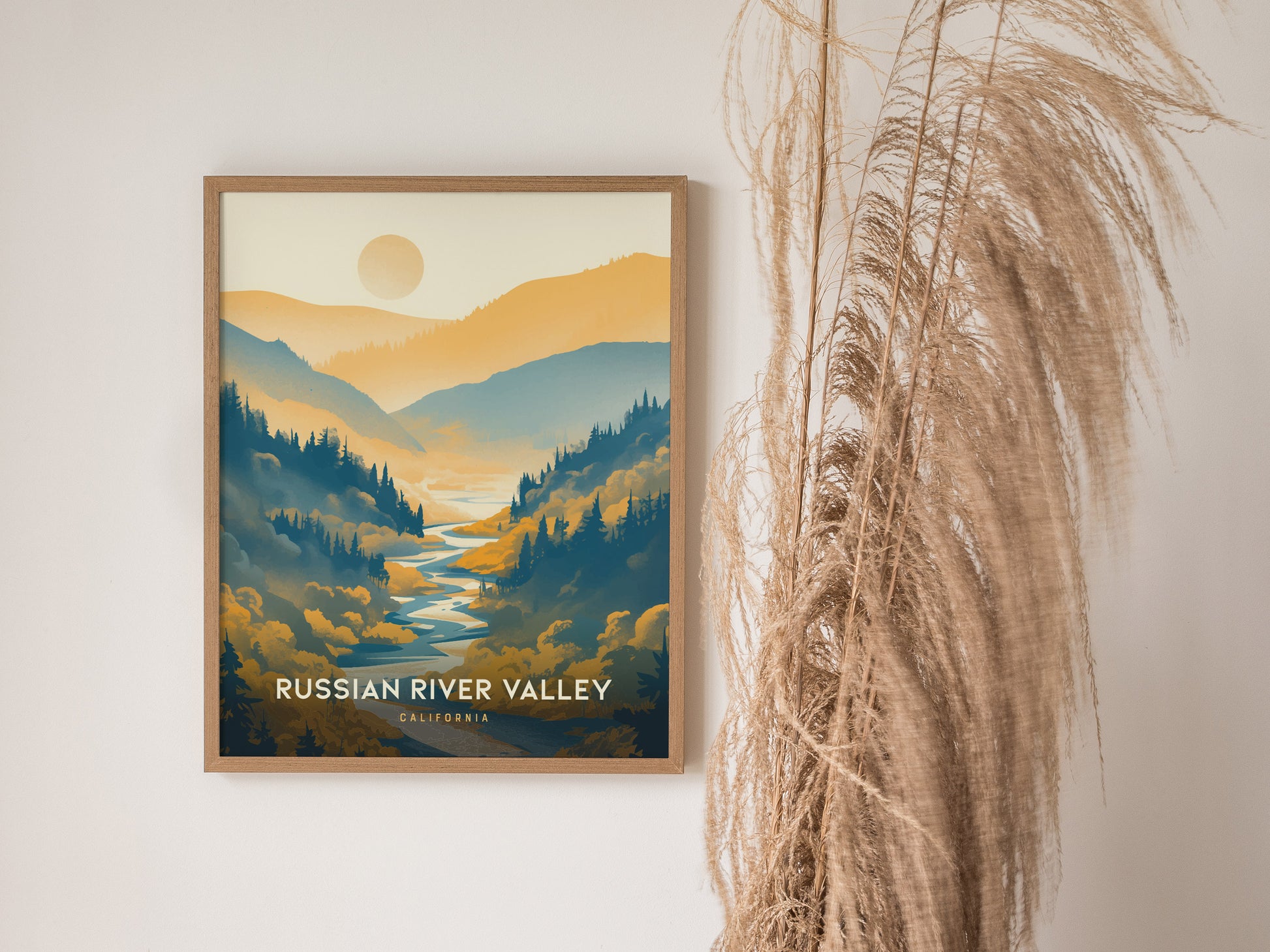 A framed poster of the Russian River Valley, featuring stylized landscapes with a river and mountains, hangs on a wall beside tall, dried grass.