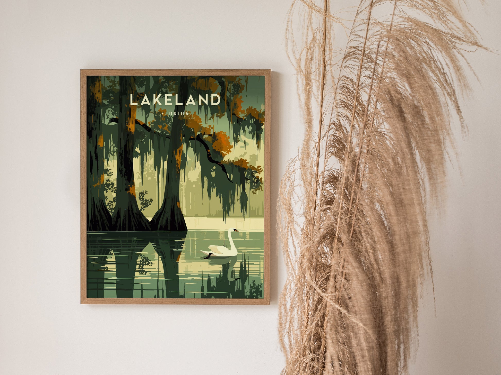 A framed poster of Lake Hollingsworth in Lakeland, Florida, featuring a serene swan on the water and lush trees, is displayed next to decorative dried grass.