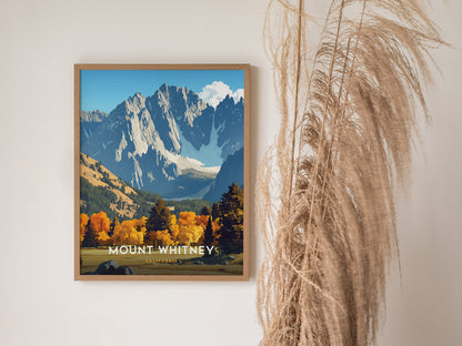 A framed poster of Mount Whitney featuring dramatic granite ridgelines and vibrant autumn foliage, set against a clear blue sky, hangs on a wall beside dry pampas grass.