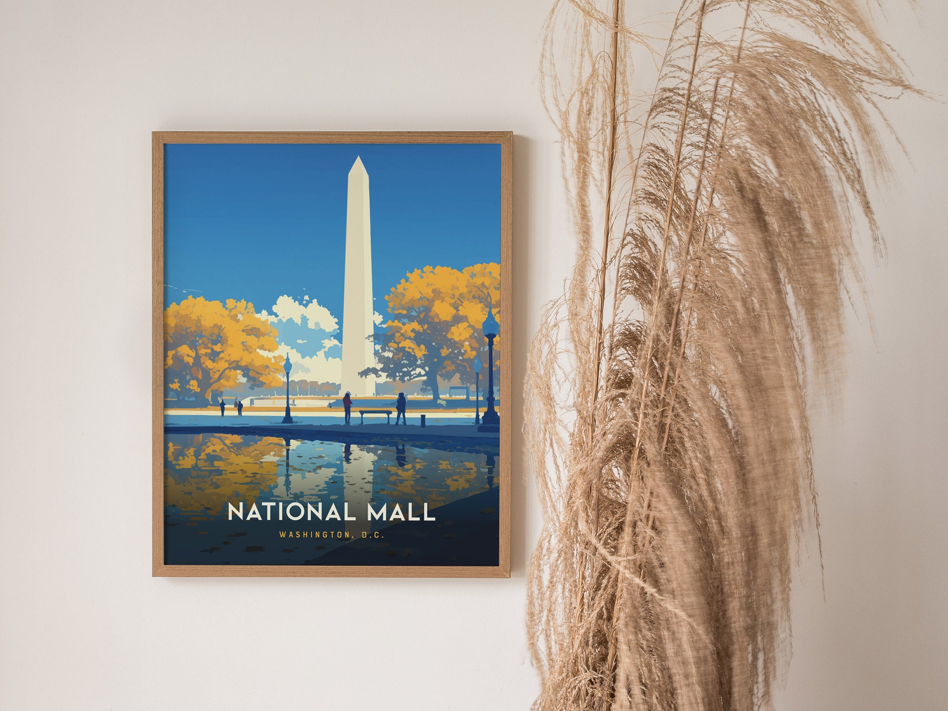 A framed poster of the National Mall in Washington, D.C. features the Washington Monument with autumn trees and reflections in the water. Decorative dried plants are placed beside it.