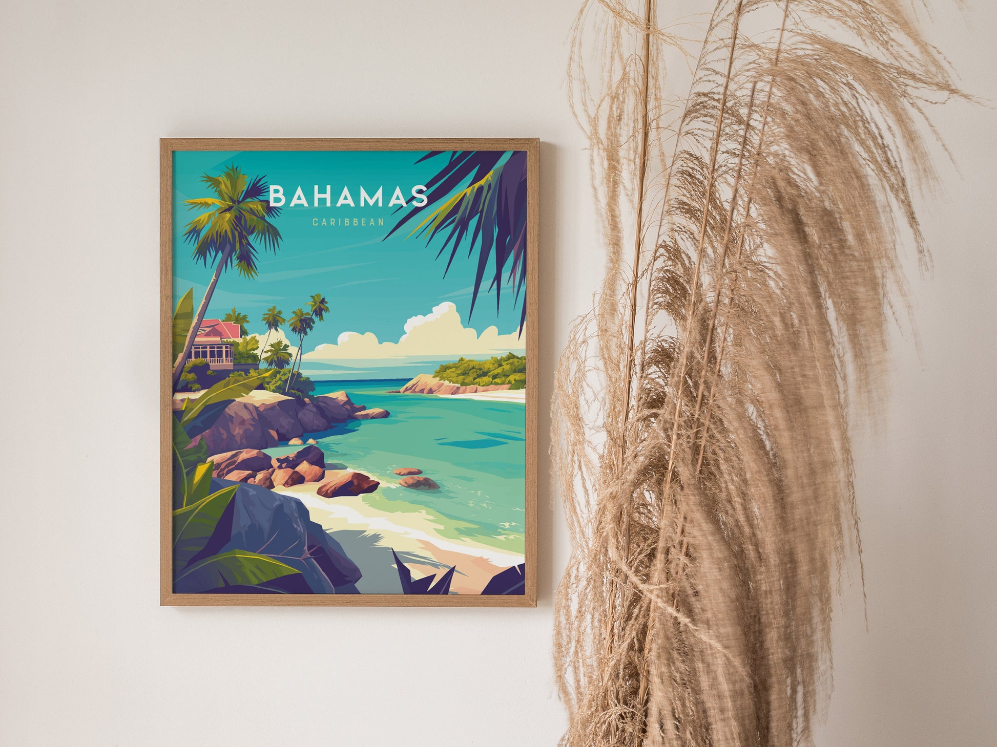 A framed Bahamas travel poster features a vibrant tropical scene with turquoise waters, palm trees, and rocky shores. Dried pampas grass is placed beside it for decoration.