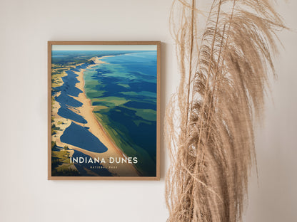 A framed poster of Indiana Dunes National Park hangs on a wall beside tall, dried pampas grass. The artwork depicts a scenic shoreline with vibrant blue.