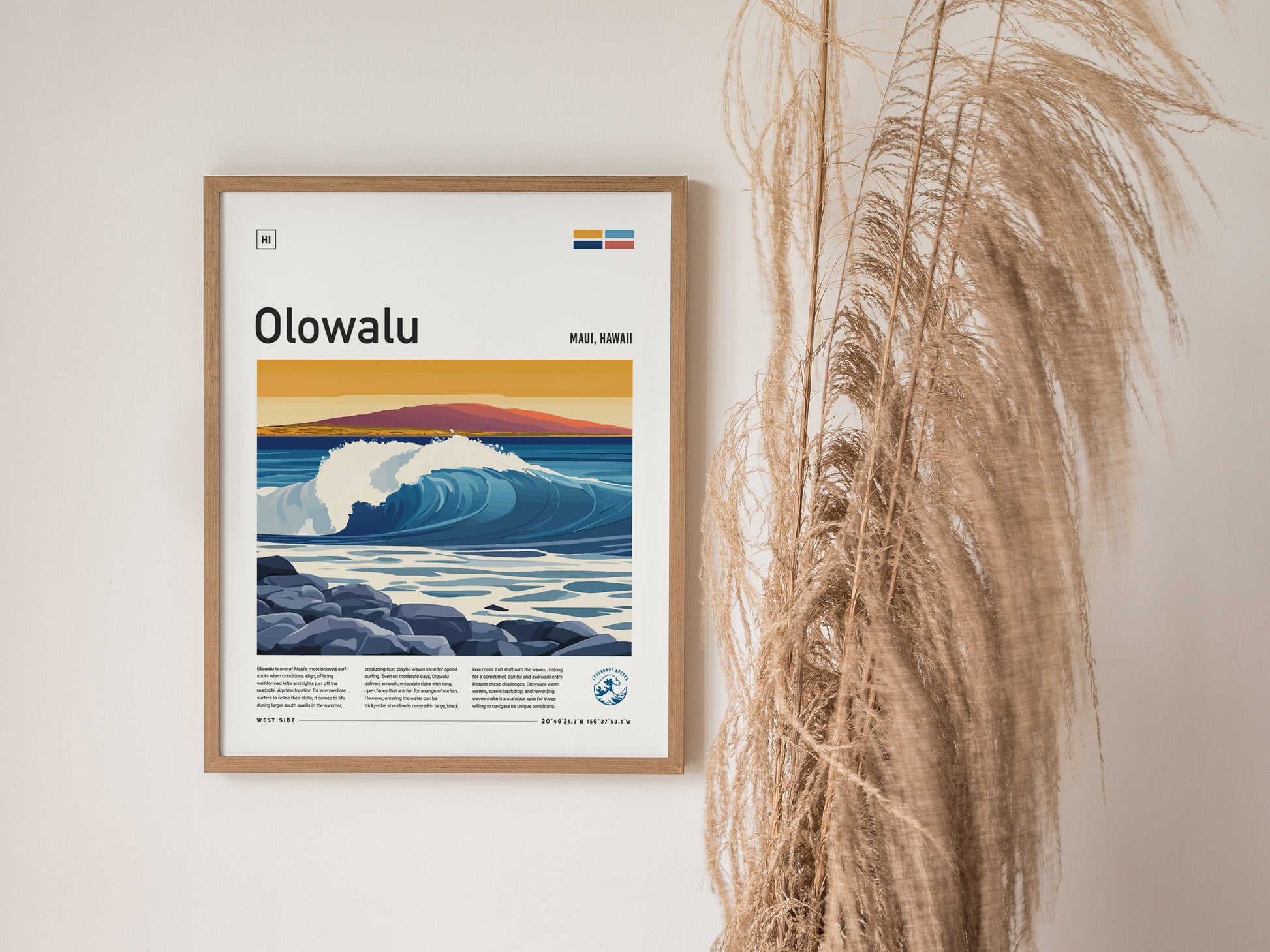A framed Olowalu Maui surf poster featuring vibrant ocean waves and a mountainous sunset is displayed on a wall next to decorative pampas grass.