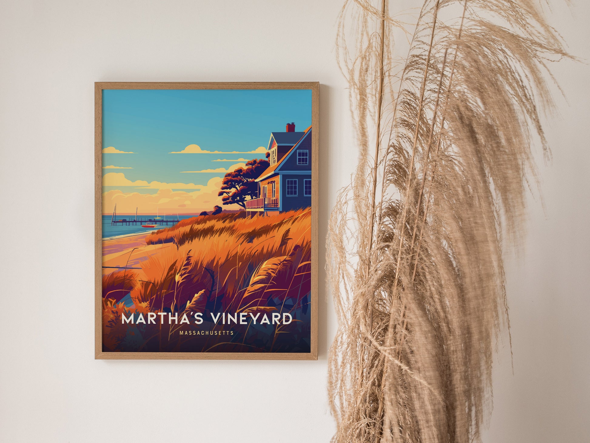 Framed Marthas Vineyard poster featuring a coastal scene with a house, golden grasses, and sailboats on the horizon, displayed on a wall next to decorative pampas grass.