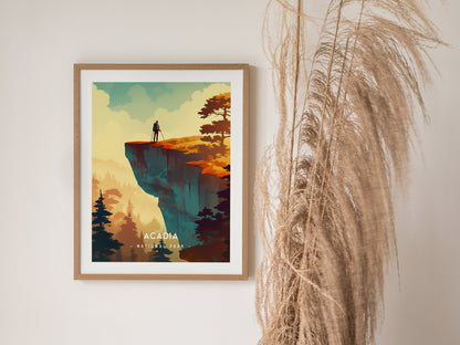A framed minimalist poster of Acadia National Park features a person standing on a cliff, surrounded by trees and a vibrant sky. Pampas grass decorates the wall beside it.