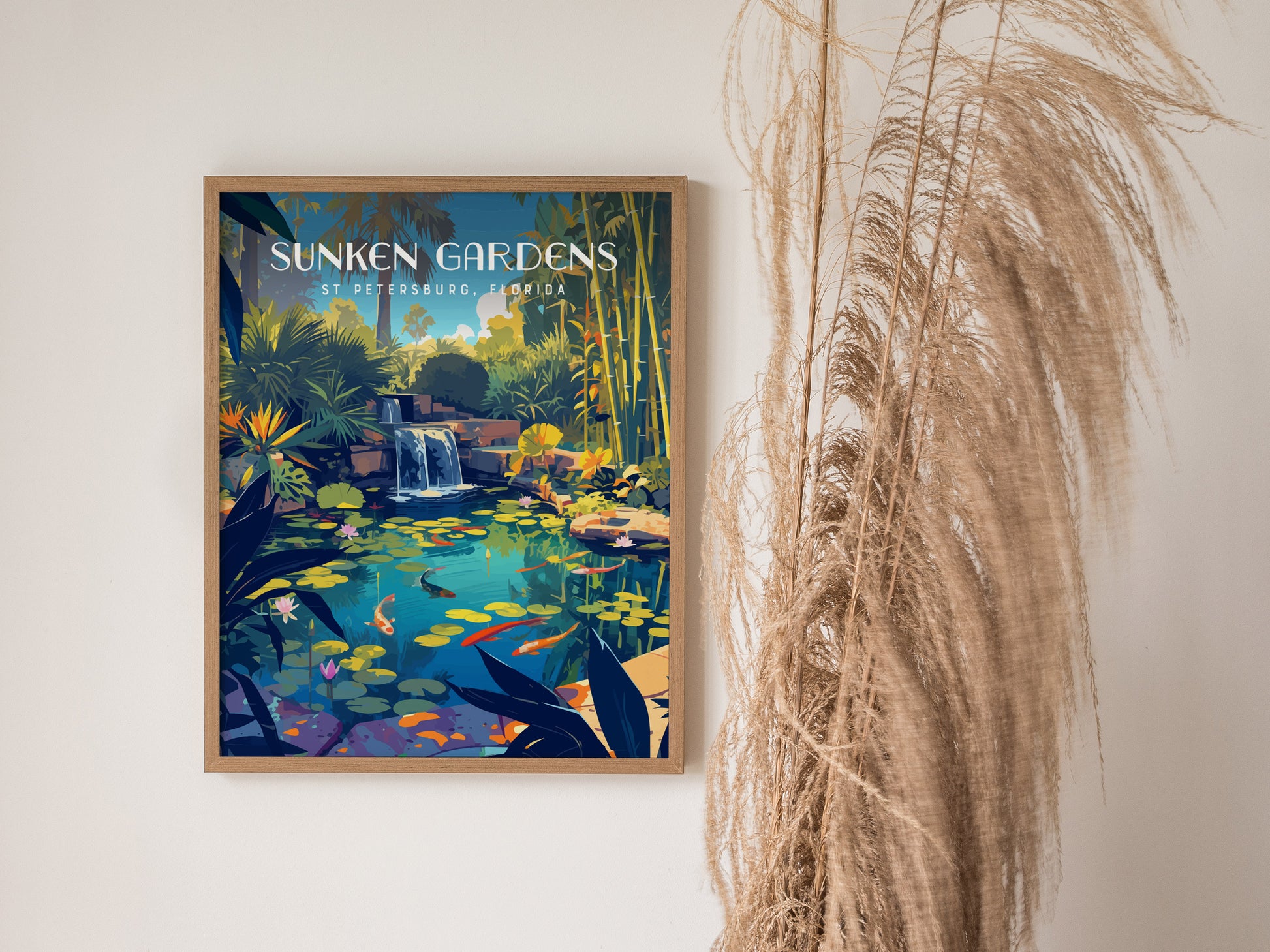 A framed poster of Sunken Gardens in St. Petersburg, Florida, featuring a vibrant koi pond and lush tropical foliage, is displayed next to tall, dried ornamental grass.