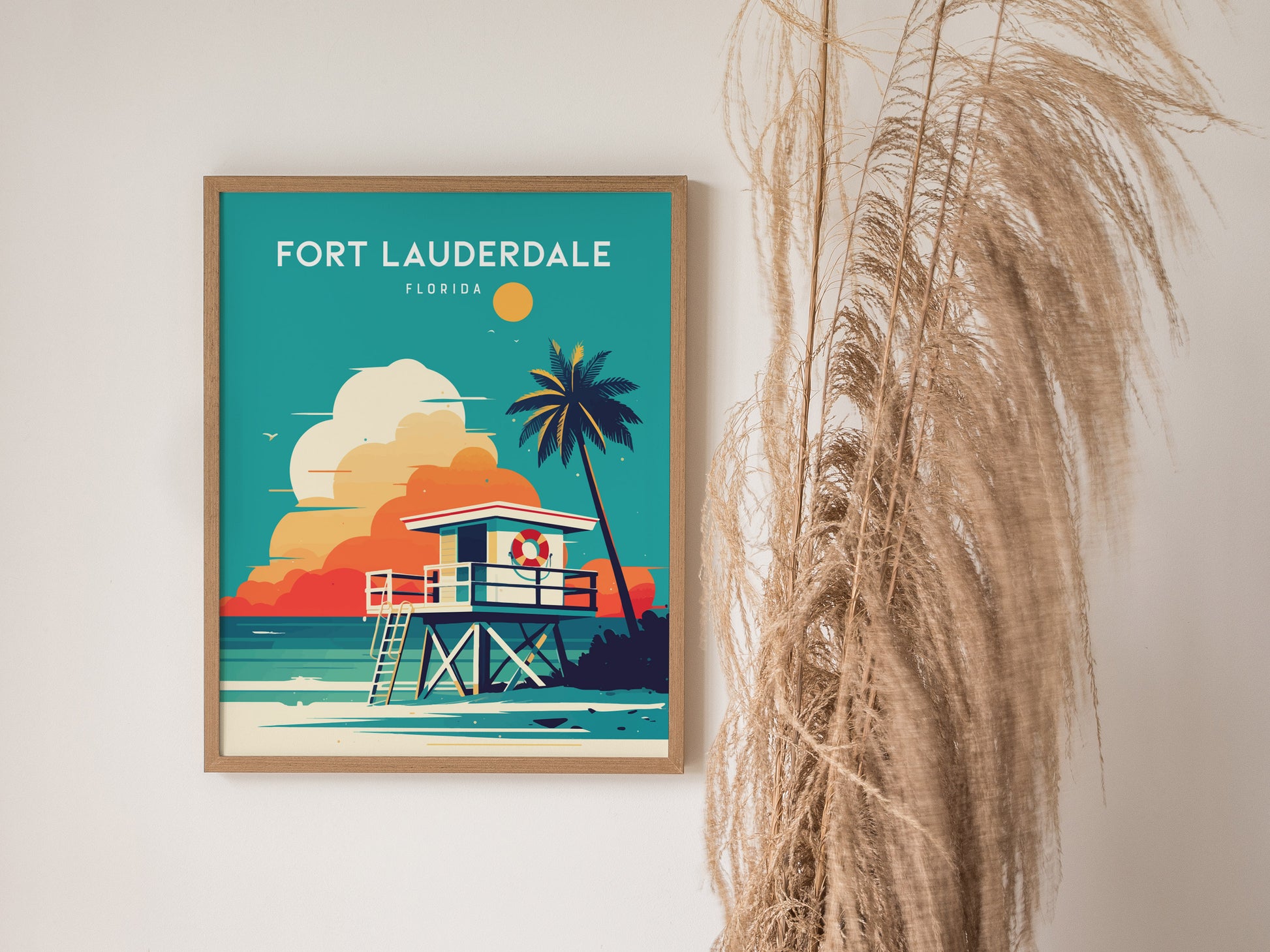 A framed Fort Lauderdale poster features a lifeguard stand and palm tree against a vibrant beach backdrop. Dried pampas grass decorates the wall beside the artwork.