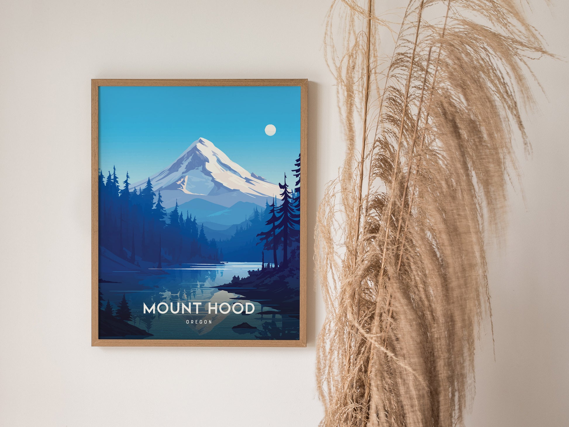Framed Mount Hood poster depicting a snow-capped mountain with surrounding forest and lake, set against a bright blue sky. Pampas grass decorates the right side of the image.