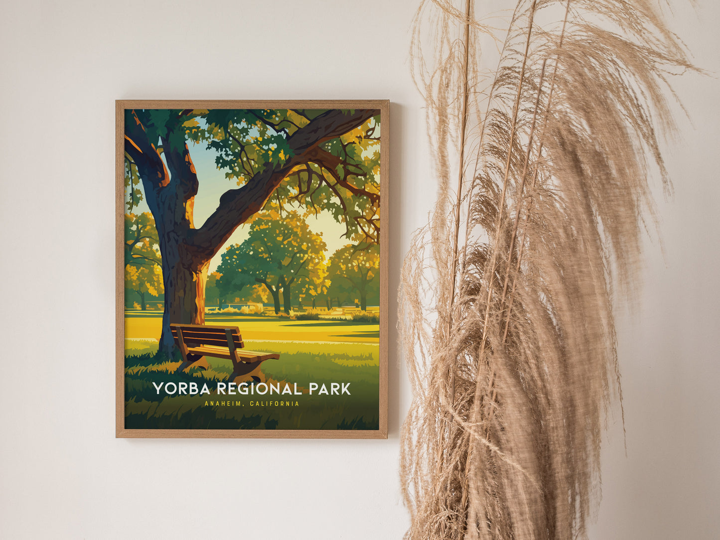 A framed Yorba Regional Park poster is displayed on a wall, showing a sunlit park scene with a bench and trees. Tall dried grasses are positioned beside it.