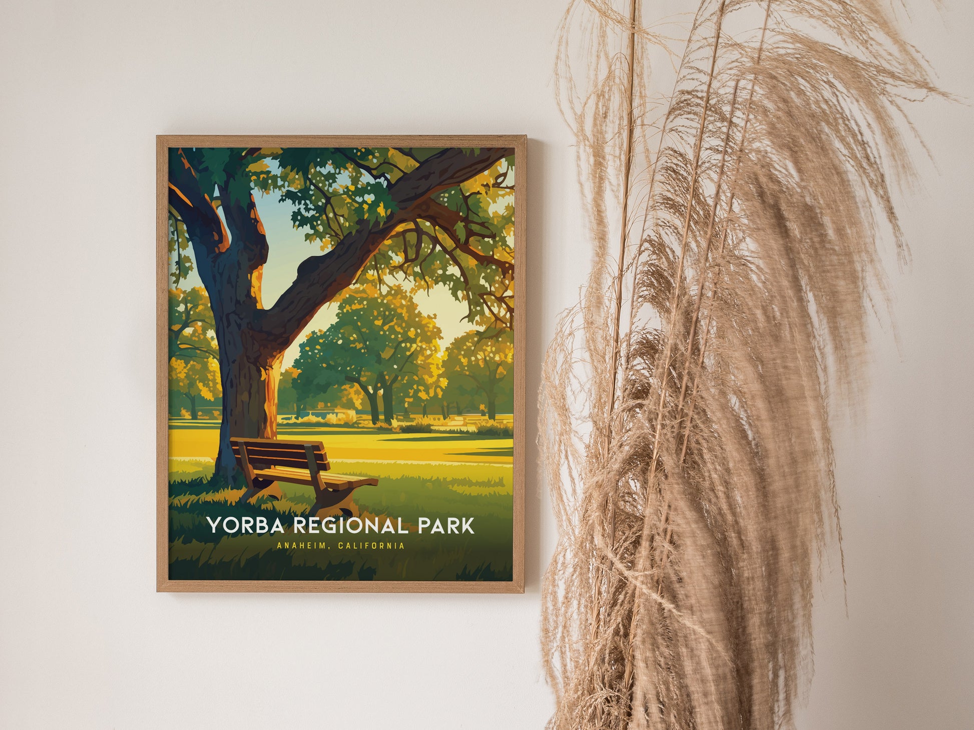 A framed Yorba Regional Park poster is displayed on a wall, showing a sunlit park scene with a bench and trees. Tall dried grasses are positioned beside it.