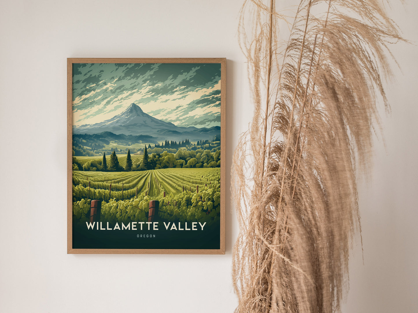 A framed poster of Willamette Valley, Oregon, features lush vineyards and a distant mountain, displayed on a wall beside tall, dried grasses.