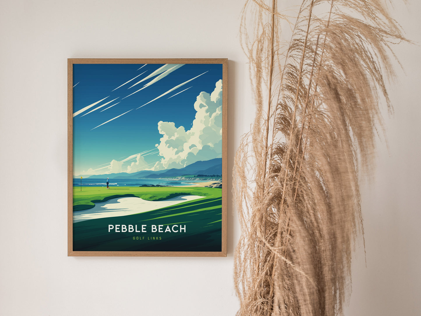 Framed poster of Pebble Beach Golf Links featuring a vibrant coastline and golf course against a blue sky, displayed next to tall, dried grasses.