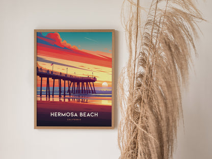 Framed Hermosa Beach poster featuring a vibrant sunset over the pier, with hues of orange, pink, and blue. Decorative dried grasses are visible on the right side.