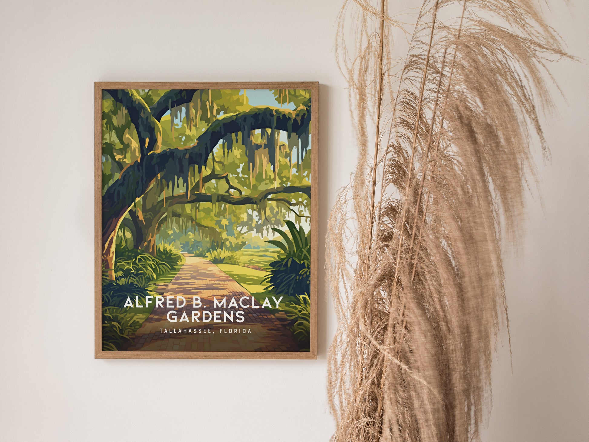 A framed poster of Alfred B. Maclay Gardens in Tallahassee, Florida, features a scenic path framed by lush green trees. Dried pampas grass decorates the adjacent wall.