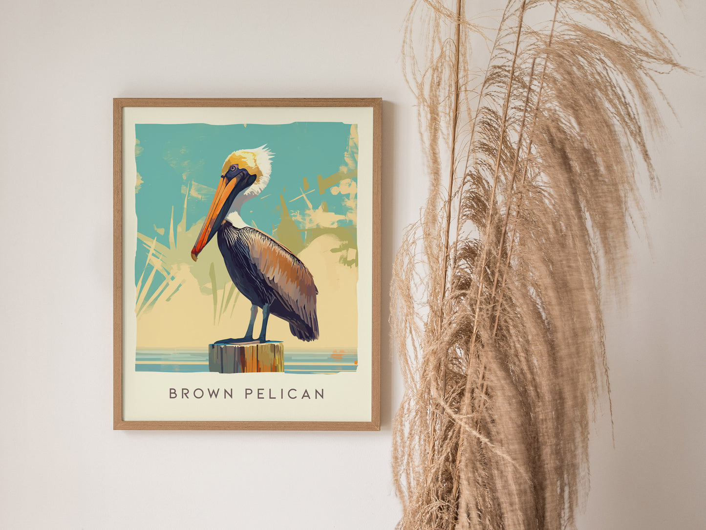 A framed poster of a brown pelican perched on a post against a stylized background is displayed next to dried pampas grass.