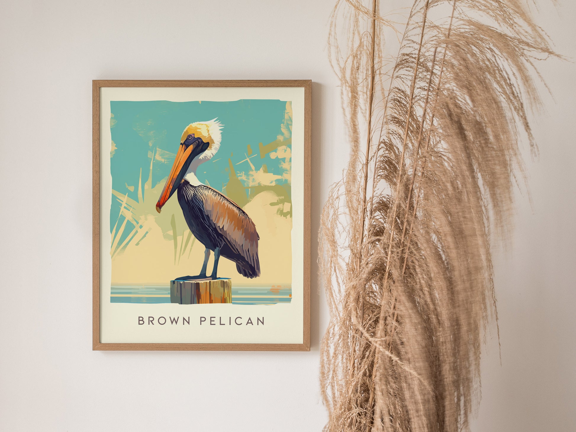 A framed poster of a brown pelican perched on a post against a stylized background is displayed next to dried pampas grass.