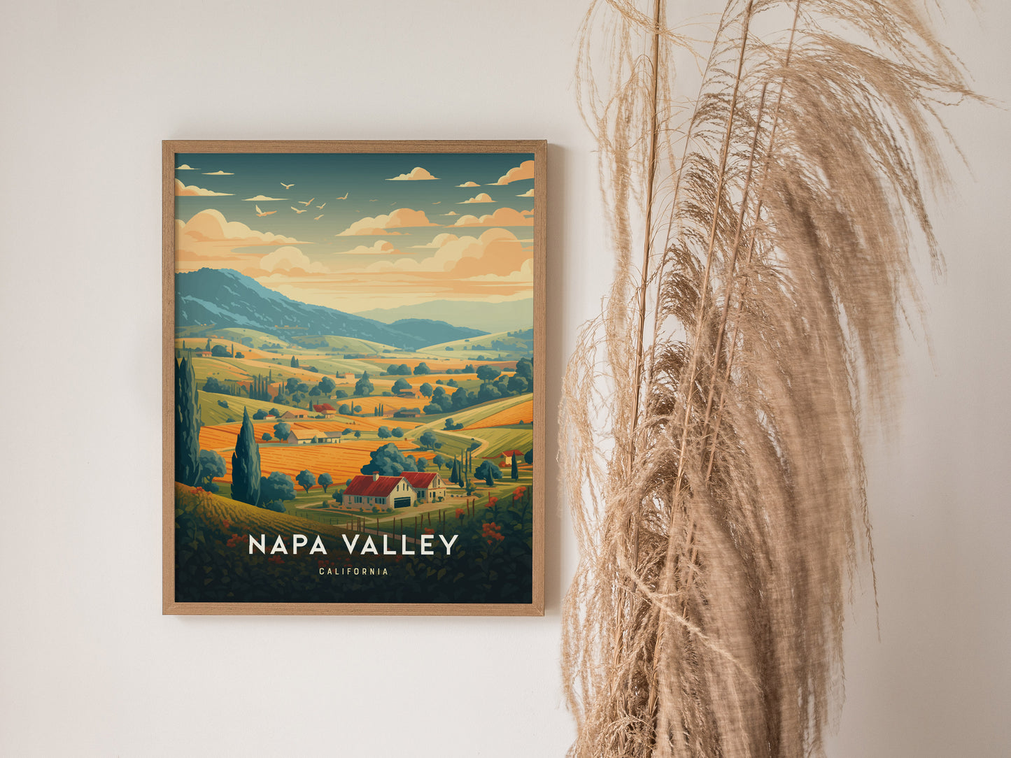 A framed Napa Valley travel poster hangs on a white wall, depicting vibrant vineyards and rolling hills under a warm sky. Tall, dried grasses stand beside it.