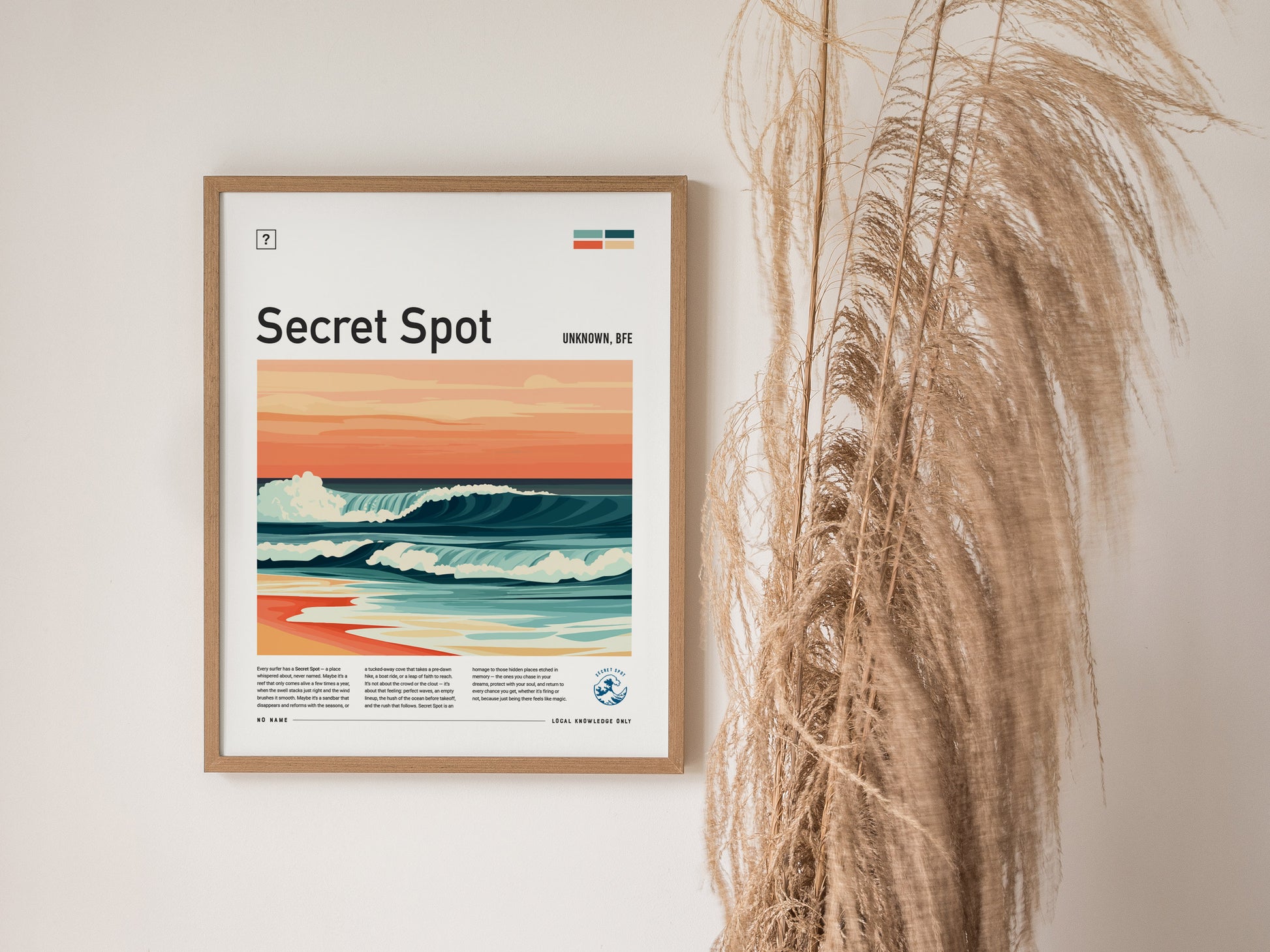 A framed surf poster titled Secret Spot features a wave under pastel skies. Its hung on a white wall beside tall, dried pampas grass.