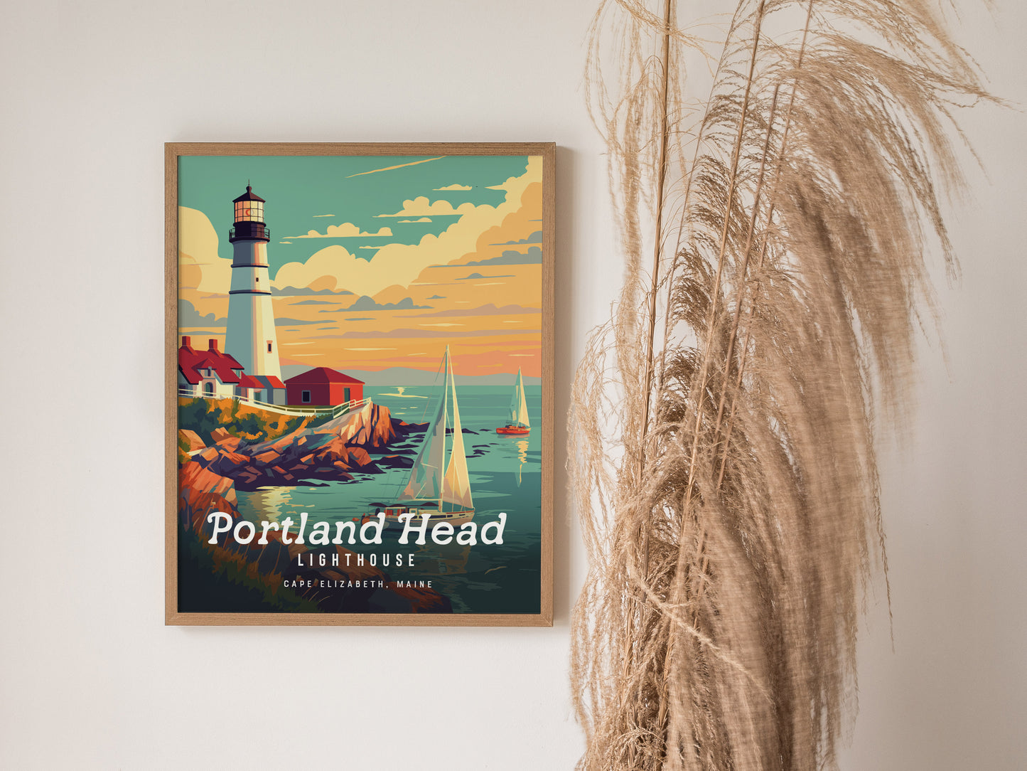 A framed poster of Portland Head Lighthouse features a vibrant sunset, rocky cliffs, and sailboats, displayed on a wall next to tall, wispy dried grasses.