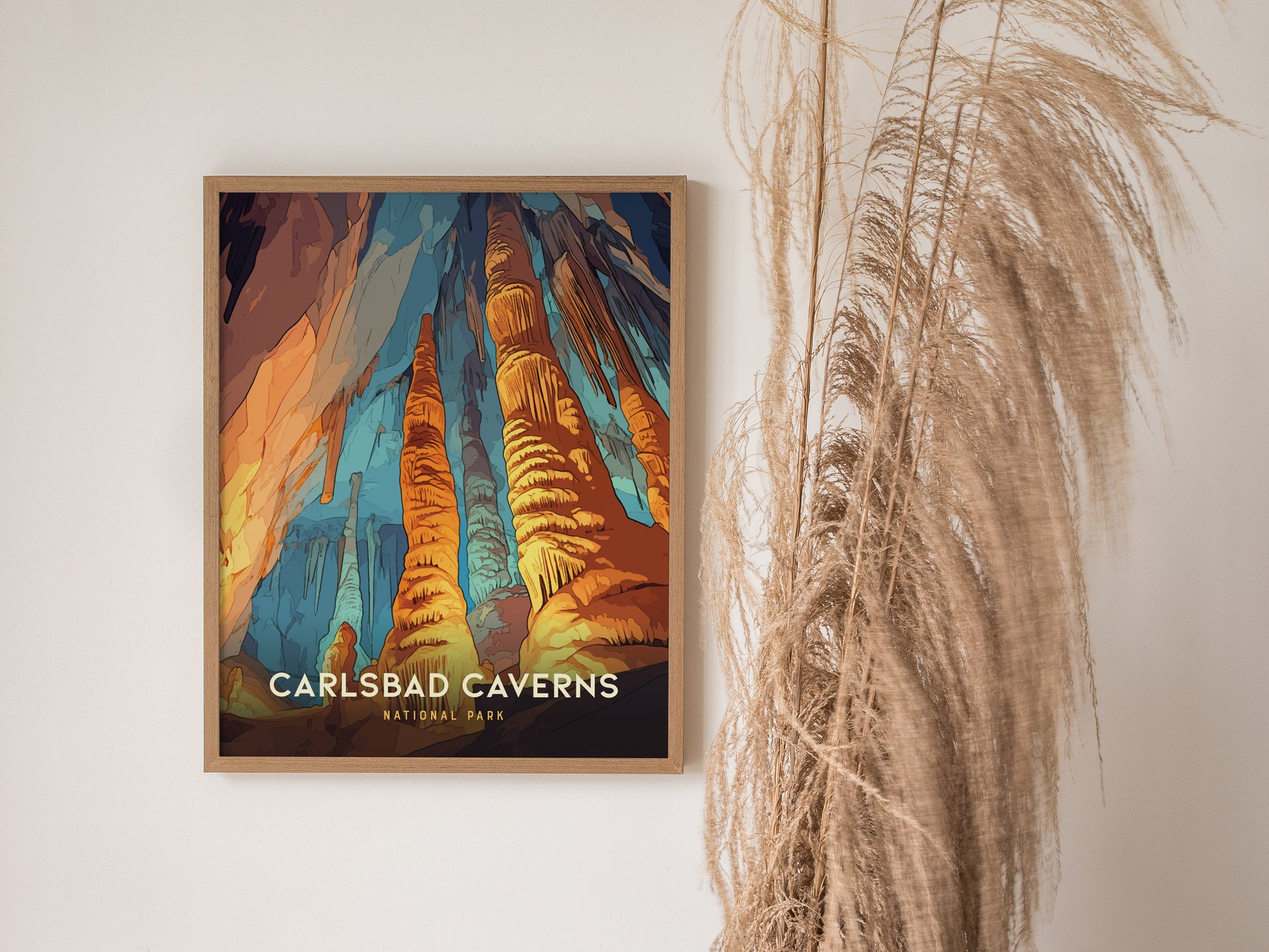 A framed Carlsbad Caverns National Park poster features vibrant rock formations against a multicolored background, displayed on a wall next to tall, wispy dried grasses.