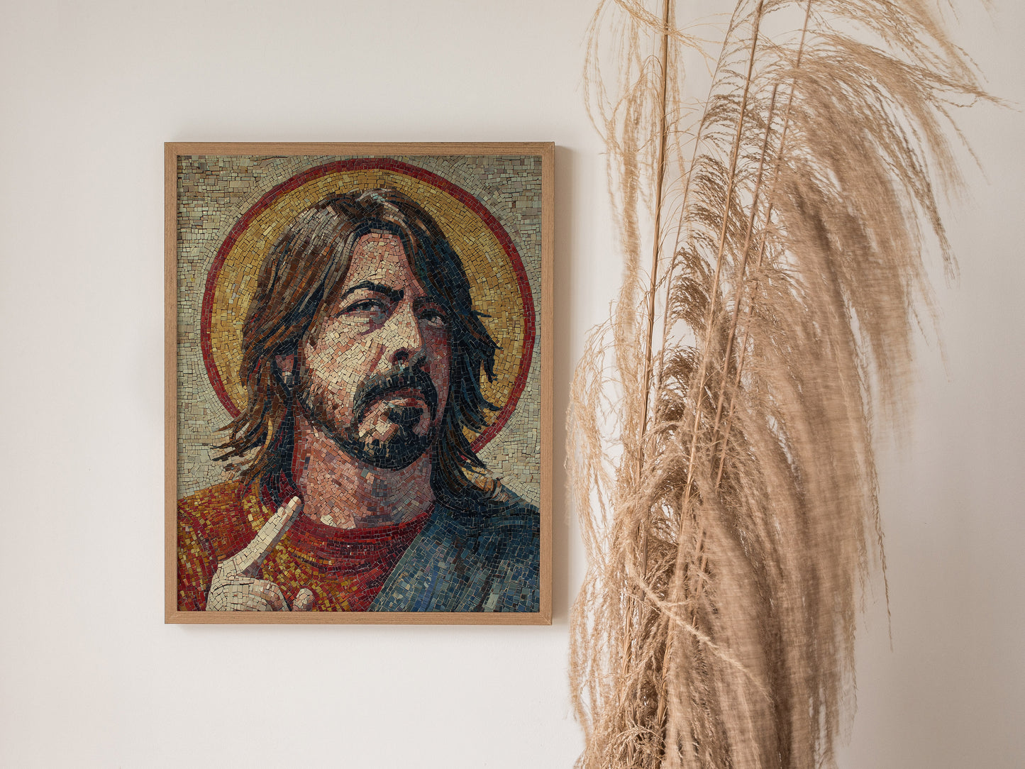 A detailed mosaic art piece featuring a male figure with long hair and a thoughtful expression, set against a golden halo. The artwork is framed in wood and displayed on a white wall, accompanied by a tall, dried pampas grass arrangement.