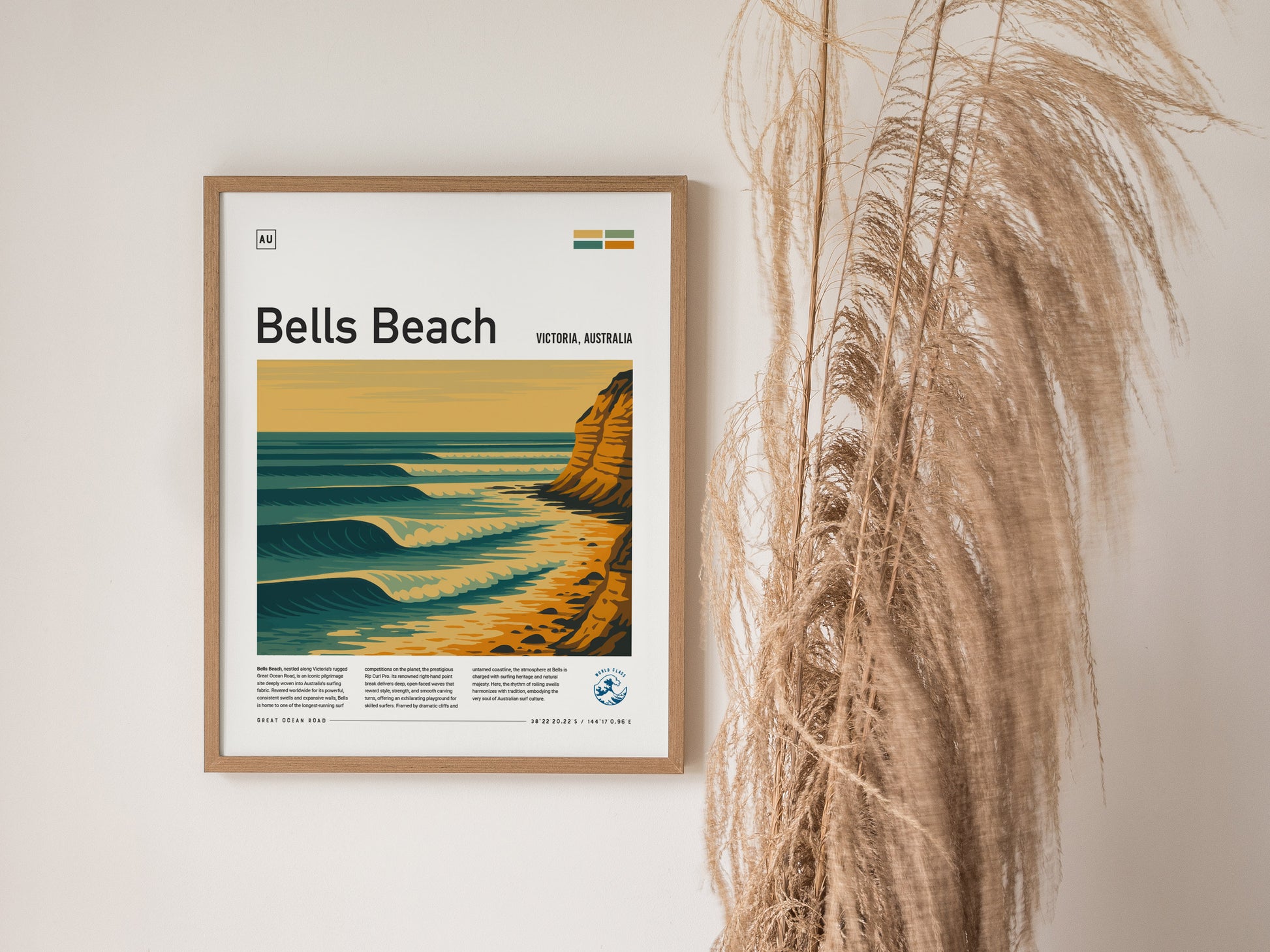 Framed poster of Bells Beach, Victoria, Australia, with stylized waves and cliffs, hangs on a wall beside tall dried grass. The artwork features a warm color palette.
