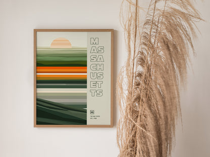 A framed poster with abstract horizontal stripes and a rising sun design, labeled Massachusetts, hangs on a wall next to dried pampas grass.