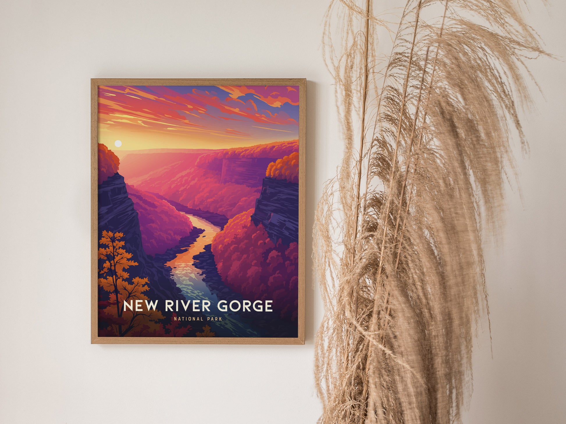 A framed poster of New River Gorge National Park features a vibrant sunset over a river, with purple and orange canyon walls, next to decorative dried grasses.