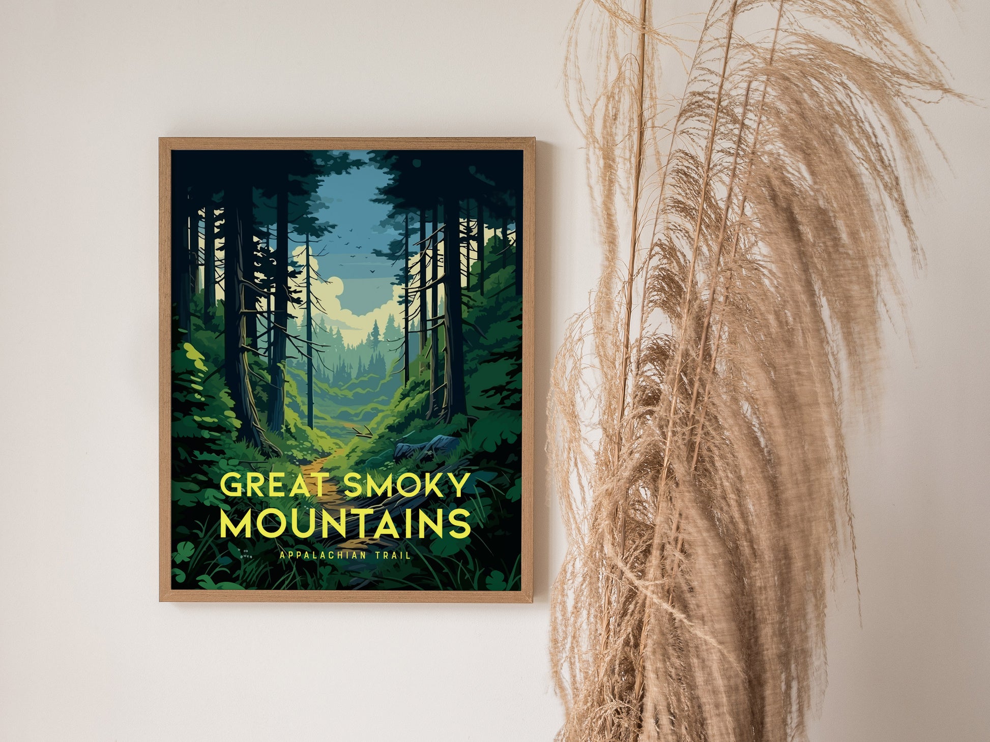 A framed poster depicting the Great Smoky Mountains with a forest path under a cloudy sky, alongside decorative dried grass on a plain wall.